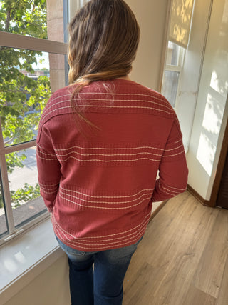 Person wearing a red jacket with white stripes indoors, looking out a window.