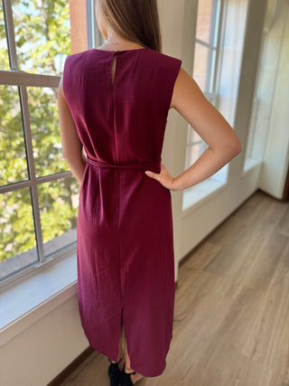 Woman wearing a burgundy dress standing by a window with natural light.