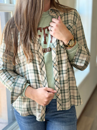 Lady standing wearing a green plaid flannel over a coffee sweatshirt.
