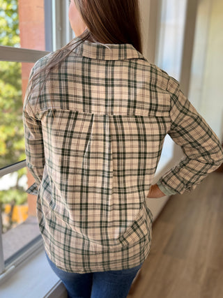Back of lady standing by a window wearing a green plaid flannel.