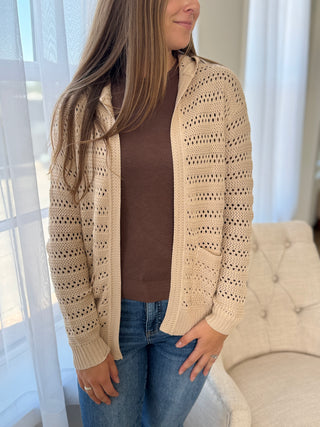 Lady standing wearing a beige hooded cardigan.
