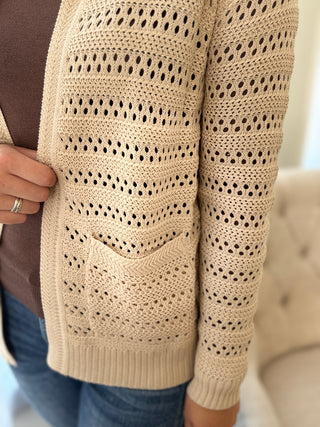 Lady standing featuring pocket of a beige hooded cardigan.