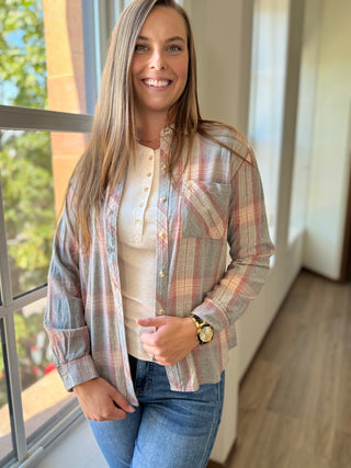 Lady standing by window wearing a grey plaid flannel over a henley shirt.