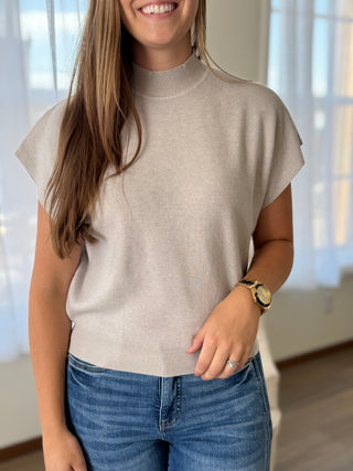 Lady standing by a window wearing a bone color mock neck lightweight sweater.