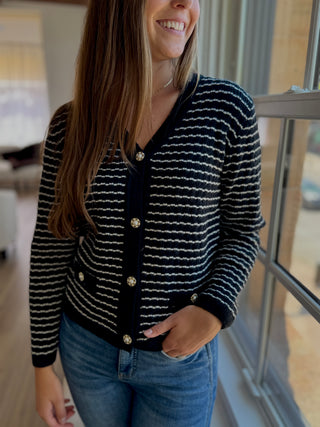 Lady standing wearing a black and white stripe button up cardigan.