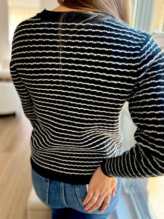 Lady standing featuring the back of the black and white button up cardigan.