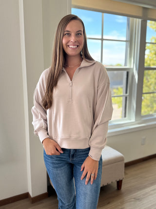 Lady standing by window featuring a taupe scuba half zip top.