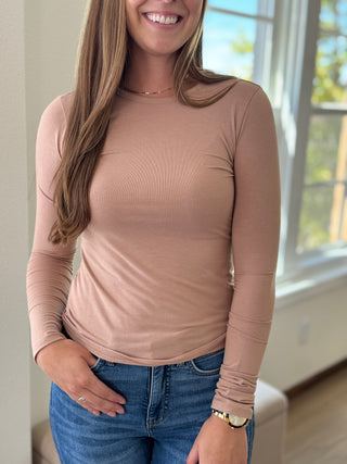 Lady standing wearing a taupe long sleeve top.