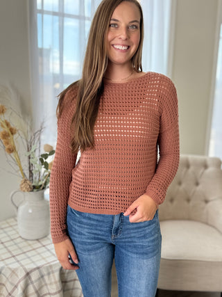 Woman wearing a brown knitted sweater and blue jeans indoors.