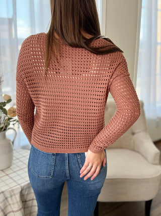 Person wearing a brown knitted sweater and blue jeans in a home setting