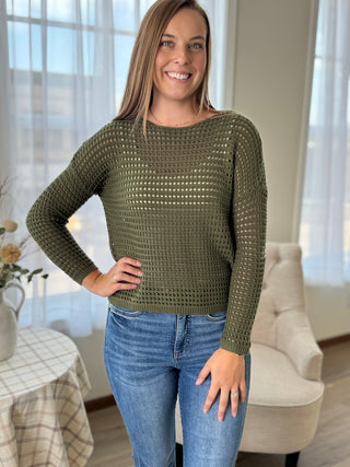 Woman wearing a green knitted sweater and blue jeans indoors.