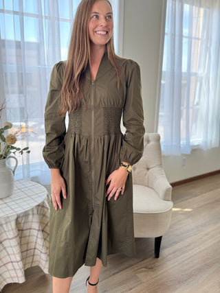 Woman wearing a green dress in a bright room with large windows.