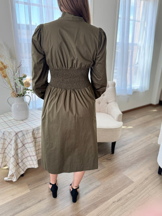 Person wearing a green dress in a room with light wood flooring and white curtains.