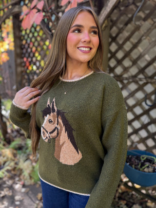 Woman in an olive horse graphic knit sweater with dark jeans | V-Rae's Boutique