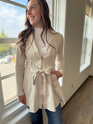 Woman wearing a beige trench coat standing by a window