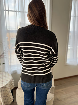 Person wearing a black and white striped sweater in a room with curtains.