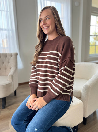 Woman wearing a brown and white striped sweater sitting on a chair in a living room.