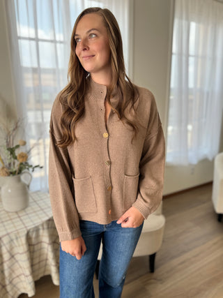 Woman wearing a beige cardigan and blue jeans indoors.