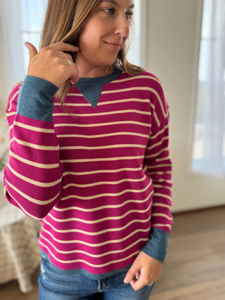 Person wearing a striped sweater with blue sleeves and collar indoors.