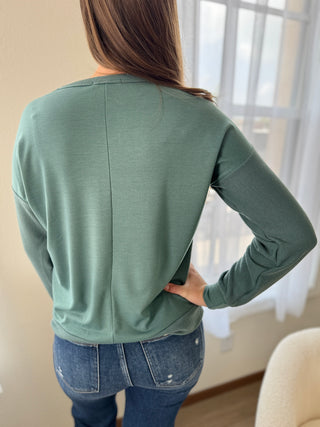 Person wearing a green long-sleeve top and blue jeans indoors.