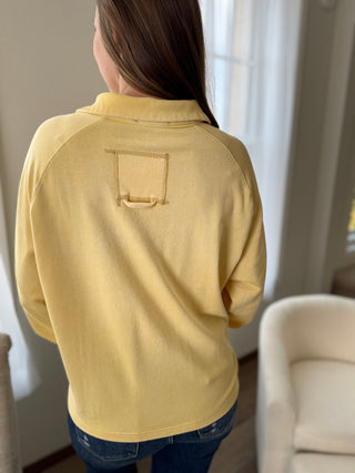 Person wearing a yellow long-sleeve shirt with a pocket detail, standing indoors.
