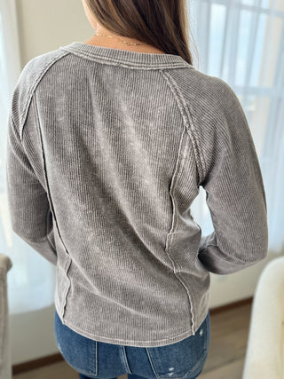 Person wearing a gray ribbed sweater in a room with light-colored walls.