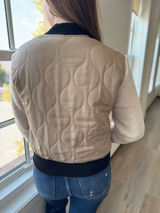 Person wearing a beige quilted jacket with a black waistband indoors.