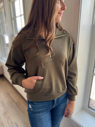 Woman wearing an olive green pullover with a window in the background