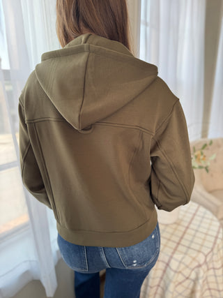 Person wearing a green hoodie in a room with curtains and a bed.