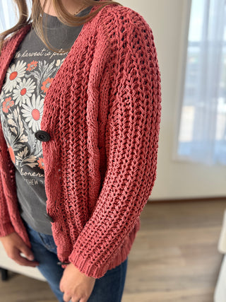 Person wearing a textured red cardigan over a graphic t-shirt indoors.