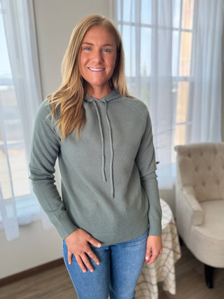Photo of a woman smiling wearing a knit hoodie top. 