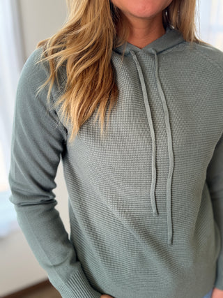 Photo of a woman smiling wearing a knit hoodie top. 