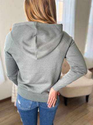 Photo of a woman smiling wearing a knit hoodie top. 