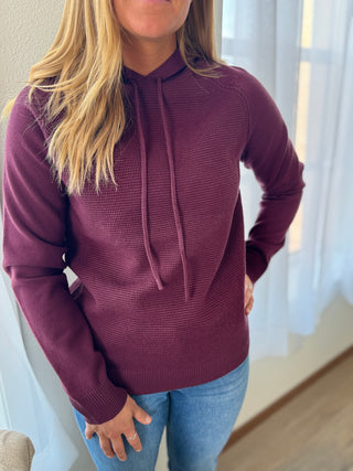Photo of a woman smiling wearing a knit hoodie top. 