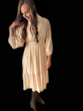 Woman wearing a beige dress with long sleeves against a black background