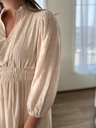 Beige dress with long sleeves worn by a person, blurred background