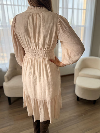 Person wearing a beige dress in a room with white curtains and furniture.