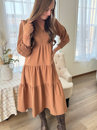Woman wearing a brown dress in a room with a bed and chair.