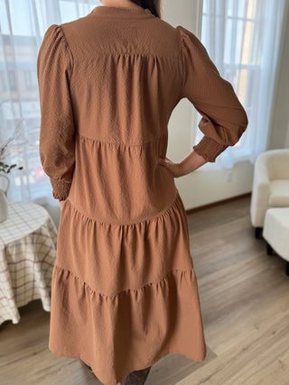 Person wearing a brown dress in a room with light wood flooring and white furniture.