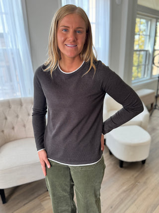 Woman wearing a dark gray long-sleeve shirt and green pants in a living room.