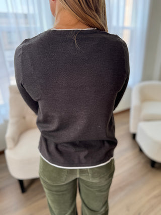 Person wearing a dark gray sweater and green pants in a room with light-colored furniture.
