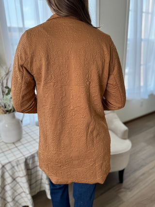 Person wearing a brown textured cardigan in a room with a table and chair.