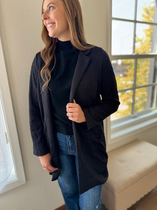 Woman wearing a black coat indoors with a window in the background