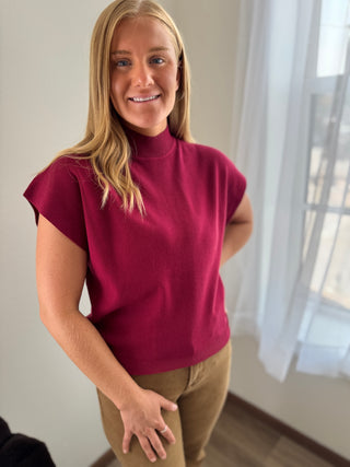 Woman wearing a maroon turtleneck top in a room with a window.