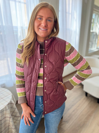 Woman wearing a striped sweater and quilted vest indoors.