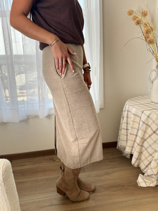 Person wearing beige wide-leg pants and brown boots in a room with a bed and window.
