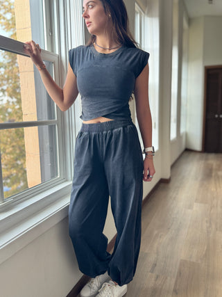 Woman in a gray outfit standing by a window in a well-lit room.