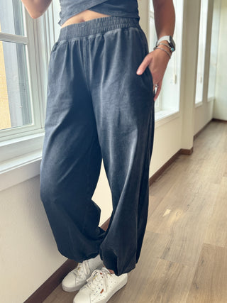 Person wearing blue sweatpants and white sneakers in a room with large windows.