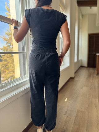 Person wearing a dark outfit standing by a window in a well-lit room.