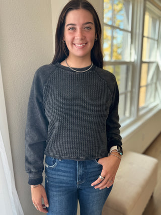 Person wearing a dark gray textured sweater and blue jeans indoors.